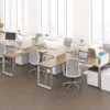 Studio photography of AMQ's Icon Benching. There is two 6-Pack single run workspaces, each with a green cushioned chair placed at the desk. It is using a walnut laminate. Another part of the desk juts out. The sun is shining in from the window beyond.