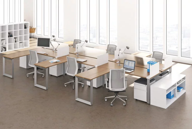 Studio photography of AMQ's Icon Benching. There is two 6-Pack single run workspaces, each with a green cushioned chair placed at the desk. It is using a walnut laminate. Another part of the desk juts out. The sun is shining in from the window beyond.