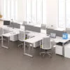 Studio photography of AMQ's Icon Benching. There is two 6-Pack single run workspaces, each with a green cushioned chair placed at the desk. It is using the white laminate. Another part of the desk juts out. The sun is shining in from the window beyond.