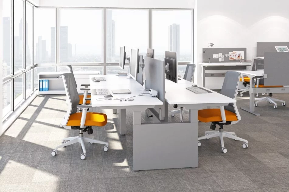 Studio photography of AMQ's KINEX Benching. A 2-Pack double run workspace is at the corner by the window. Another pair of single run is off to the side. Each has a white laminate table top, and adjustable screens.