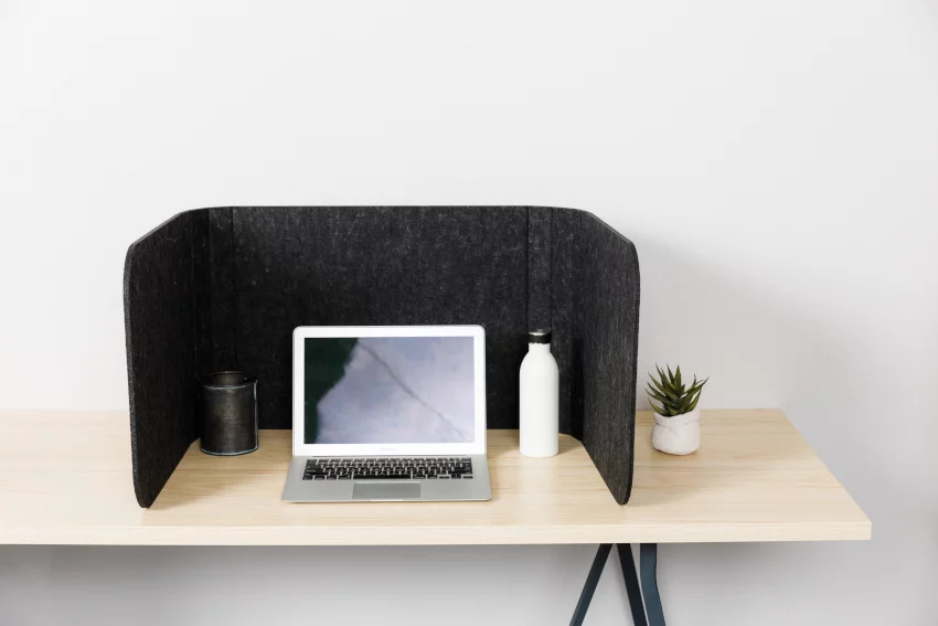 Hide privacy screen, using charcoal colored PET. A laptop is open, with a plant to the right side of the Hide screen's wall.