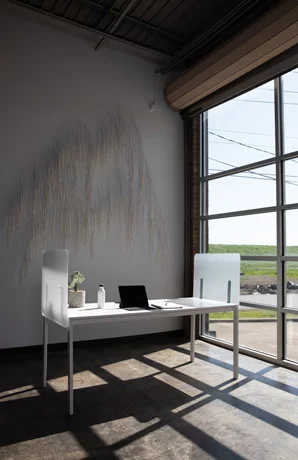 Simple table desk placed at the window in an office. Shelter screens line the desk, and a laptop sits with its lid open.