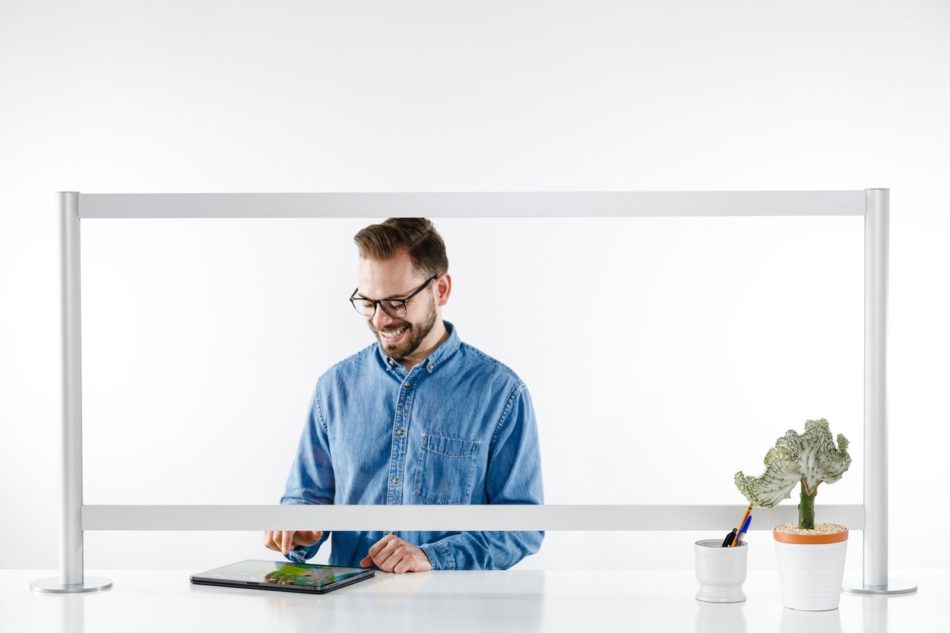 A man stands behind a counter, looking down at his tablet. A Counter Shield Classic screen separates him from the space in front.