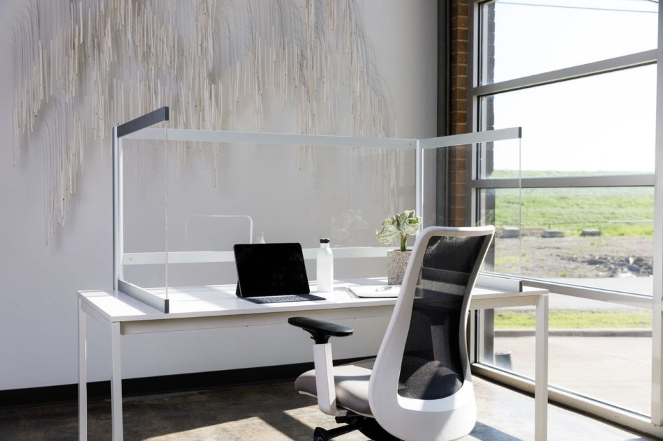 Desk Shield placed at a large window area of an open office. The Desk Shield wraps around the whole desk, and a black laptop is open.