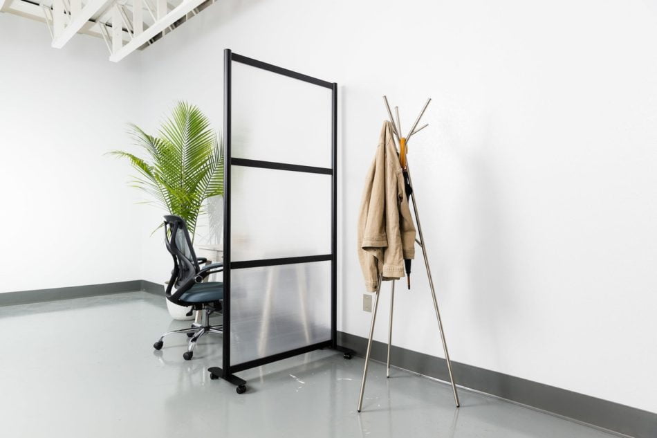 Break style Split model screen at the end of a small work table. It is using a black aluminum frame and frosted acrylic. On the other side is a tripod-style coatrack.