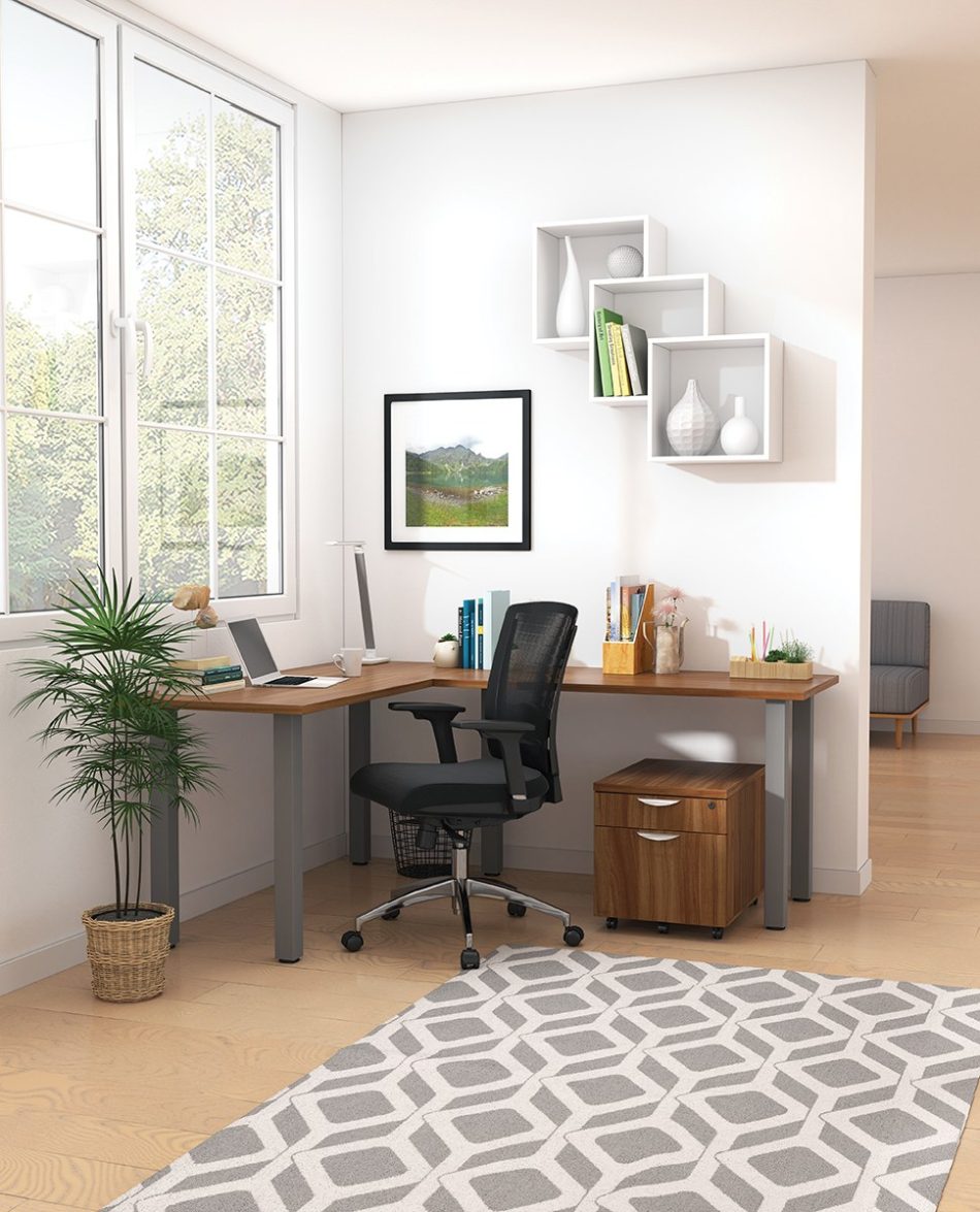 Studio shot of OTG's Home Office, with an L-shaped desk placed by the window. It has a tungsten colored metal frame and top surfaces in a Autumn Walnut finish. A matching set of drawers has been rolled under the desk, by a set of pencil cases. The office chair is seated by a laptop and an OTG LED Desk lamp in the corner.