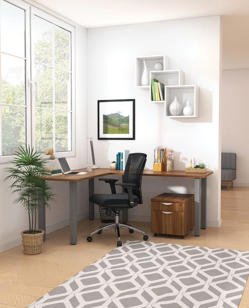 Studio shot of OTG's Home Office, with an L-shaped desk placed by the window. It has a tungsten colored metal frame and top surfaces in a Autumn Walnut finish. A matching set of drawers has been rolled under the desk, by a set of pencil cases. The office chair is seated by a laptop and an OTG LED Desk lamp in the corner.