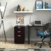 Studio shot of OTG's Home Office Setup, which has a 24" x 48" work table placed in the corner by the window. At the left is a set of pedestal drawers. The third (top) drawer has a lock on it. Both the desk and pedestal drawers are finished in an _____. A simple mesh-back office chair is pulled up to the laptop, with a LED lamp next to it.