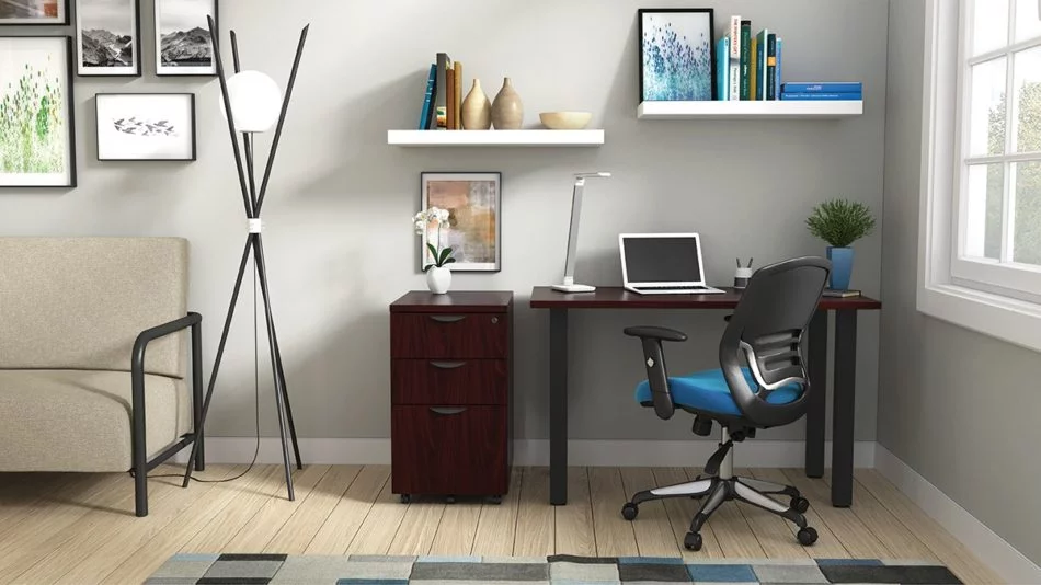Studio shot of OTG's Home Office Setup, which has a 24" x 48" work table placed in the corner by the window. At the left is a set of pedestal drawers. The third (top) drawer has a lock on it. Both the desk and pedestal drawers are finished in an _____. A simple mesh-back office chair is pulled up to the laptop, with a LED lamp next to it.