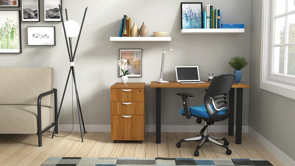 Studio shot of OTG's Home Office Setup, which has a 24" x 48" work table placed in the corner by the window. At the left is a set of pedestal drawers. The third (top) drawer has a lock on it. Both the desk and pedestal drawers are finished in an Autumn Walnut. A simple mesh-back office chair is pulled up to the laptop, with a LED lamp next to it.