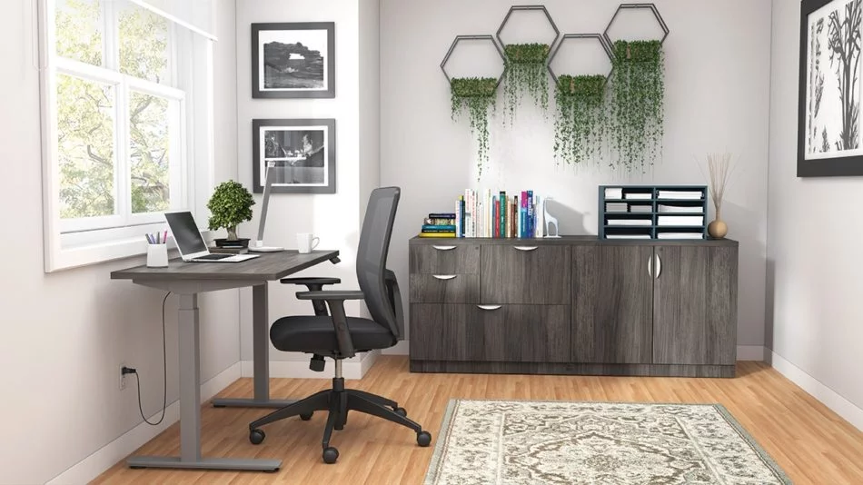Studio shot of OTG's Home Office Setup, which has a height-adjustable work desk placed at the window. A set of four planters is hung on the wall, above the mixed storage unit. Both surfaces are finished in an Artisan Grey. A total of four drawers and a double-door cabinet can store different supplies. On top is a set of books, with a giraffe bookend sculpture. A file box to the right holds two columns of slots for important files or as an Inbox.