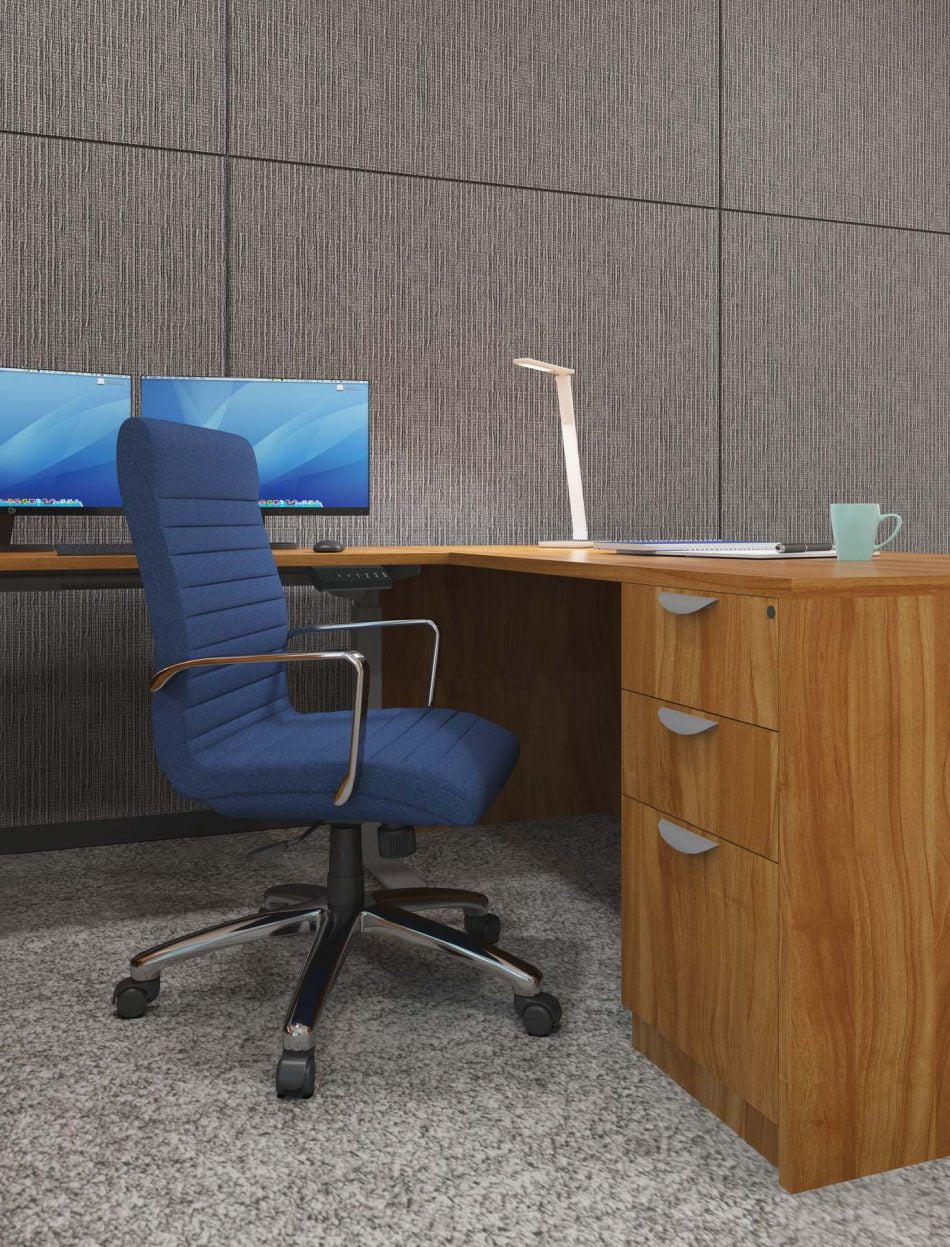 Studio photography of Offices to Go's laminate, L shaped workstation from the side. A blue high backed cushioned chair is placed at the desk, with two monitors in front.