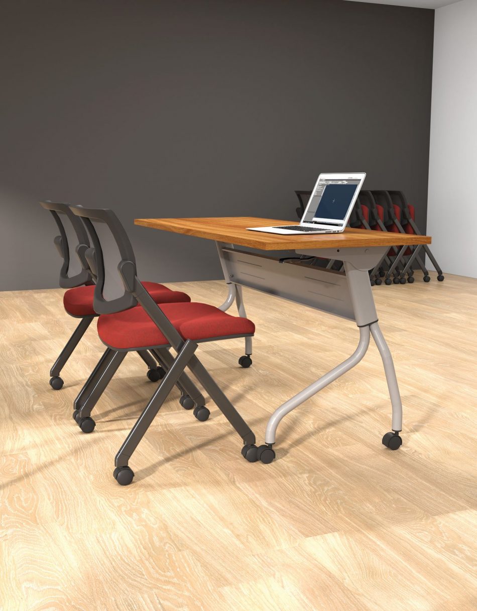 Studio photography of Offices to Go's laminate flip top training tables. The table has tungsten finished metal legs, and an Autumn Walnut laminate tabletop. Two black framed nesting chairs are placed at the table, each with a plush red cushion. A ​laptop rests on top of the table, open.