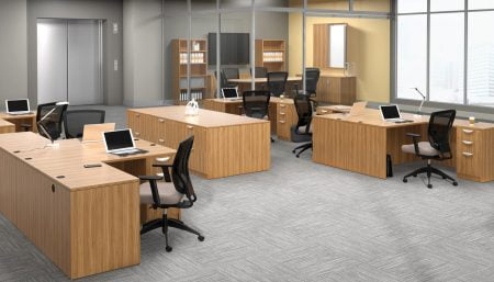 Studio photography of an Offices to Go furniture, set up in an open office near the elevator. Two L shaped desks are pressed against one another, giving a wide surface area for those passing in front. Another set like this is reversed, facing the far back wall. A large credenza exists in the wide area between these work stations. This office's desking uses an Autumn Walnut finish.