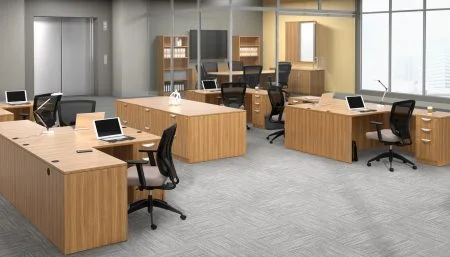 Studio photography of an Offices to Go furniture, set up in an open office near the elevator. Two L shaped desks are pressed against one another, giving a wide surface area for those passing in front. Another set like this is reversed, facing the far back wall. A large credenza exists in the wide area between these work stations. This office's desking uses an Autumn Walnut finish.