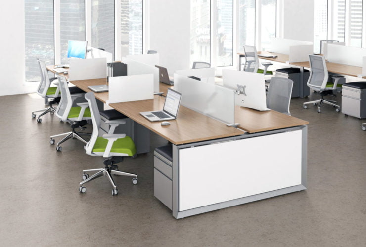 Studio photography of AMQ's Icon Benching. There is two 2-Pack double run workspaces, each with a green cushioned chair placed at the desk. The sun is shining in from the window beyond.