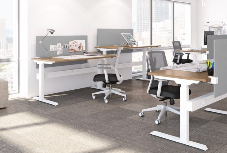 Studio photography of AMQ's KINEX Benching. Two 2-pack single run work spaces facee eachother, each table at a different level. Each one has a walnut colored laminate table top, and grey privacy screens in front of it.